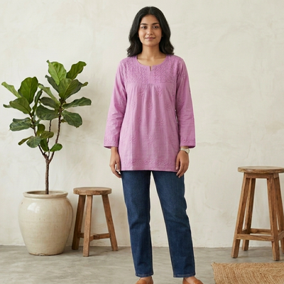 Woman wearing a purple short chikan kurti and blue jeans standing in a room with wooden stools and a plant.