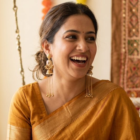 Woman wearing a mustard yellow saree with gold jewelry indoors.